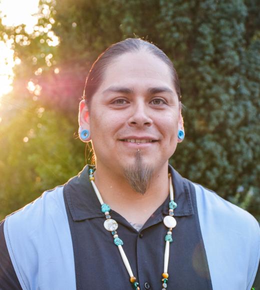 David Alvarez smiles in front of trees, illuminated by the sun behind him