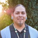 David Alvarez smiles in front of trees, illuminated by the sun behind him